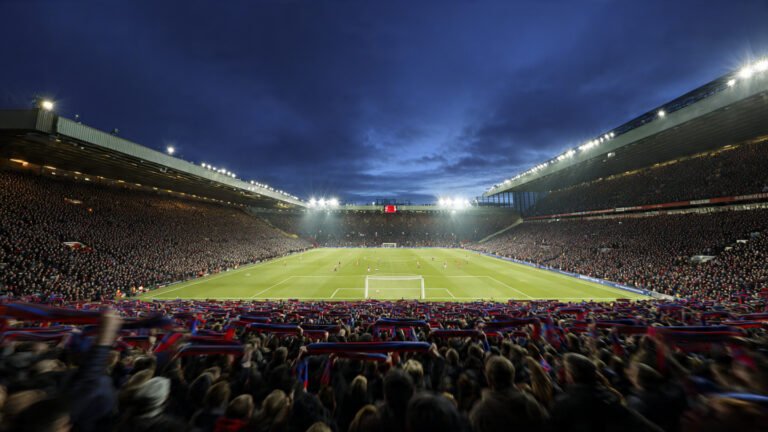 Premier League stadium packed with fans during a title race match in April 2026, floodlights illuminating the pitch at twilight