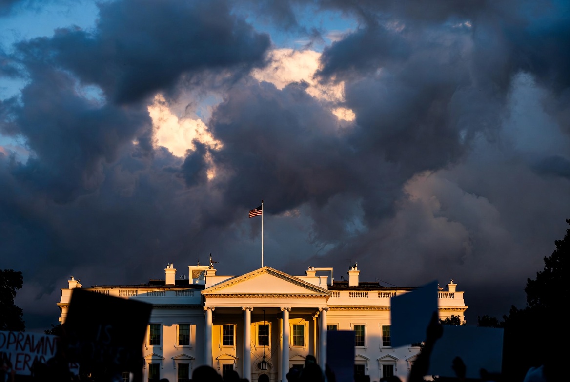 White House at dusk with storm clouds and protestors in foreground — US political crisis 2026