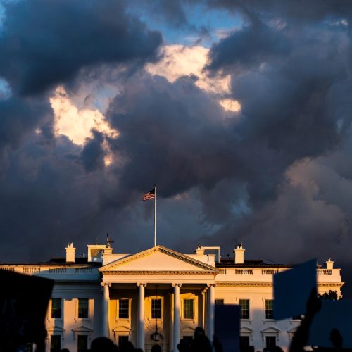 White House at dusk with storm clouds and protestors in foreground — US political crisis 2026