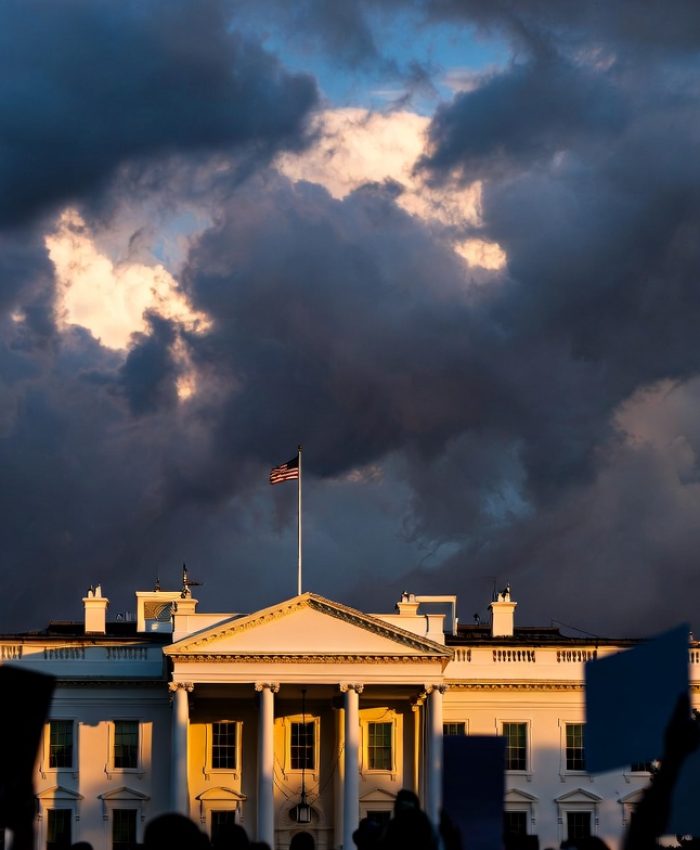 White House at dusk with storm clouds and protestors in foreground — US political crisis 2026